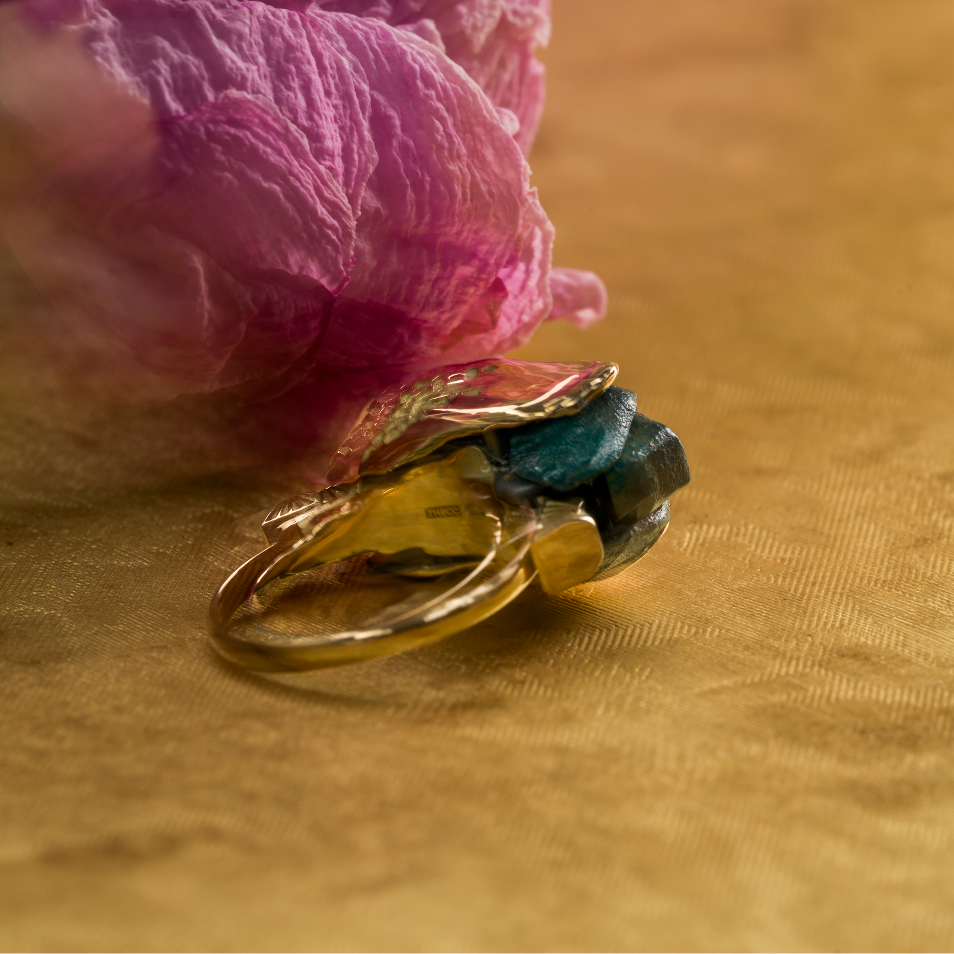Gold ring with a green gemstone on a pink flower against a gold background