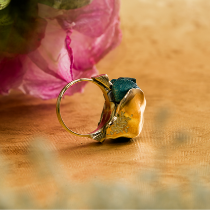 Gold ring with a green gemstone on a wooden surface with pink flowers in the background
