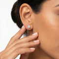 Close-up of a woman wearing a diamond stud earring with a neutral background