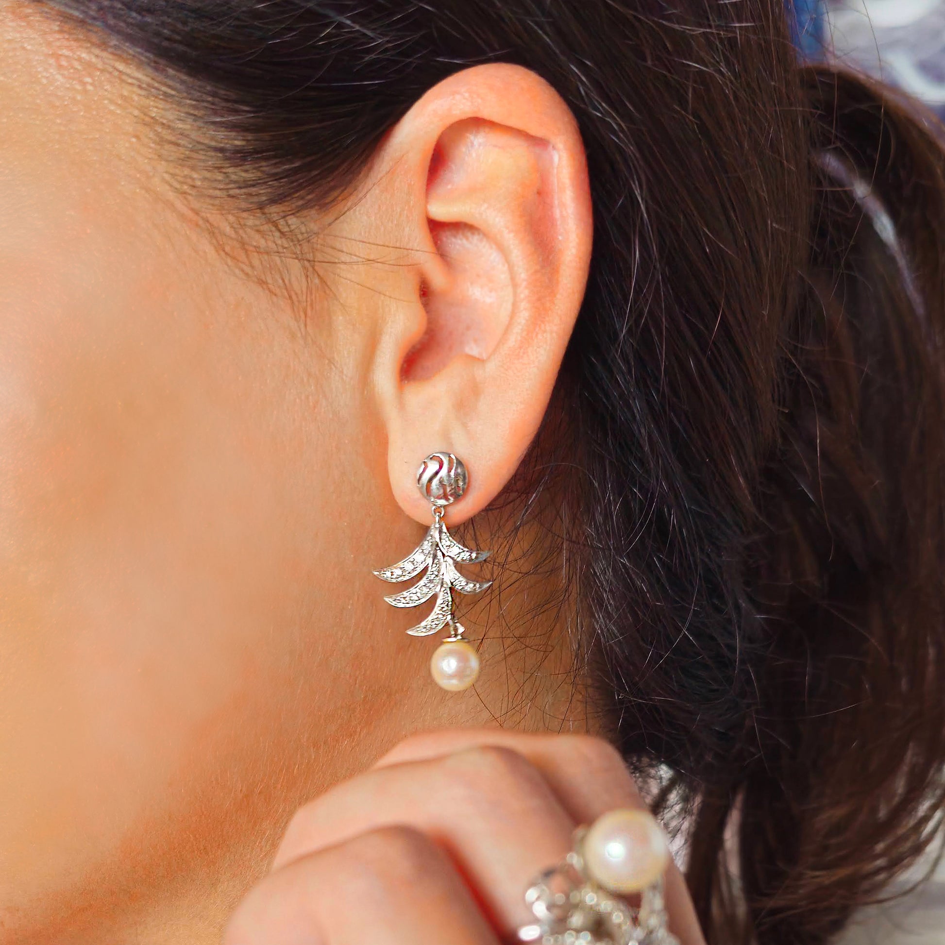 Close-up of a person wearing a gold earring with a pearl drop.