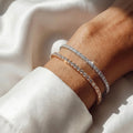 Close-up of a wrist wearing two diamond bracelets on a light background